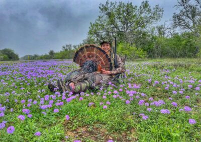 In a lush field of purple flowers, a woman relaxes beside a turkey, surrounded by the beauty of nature