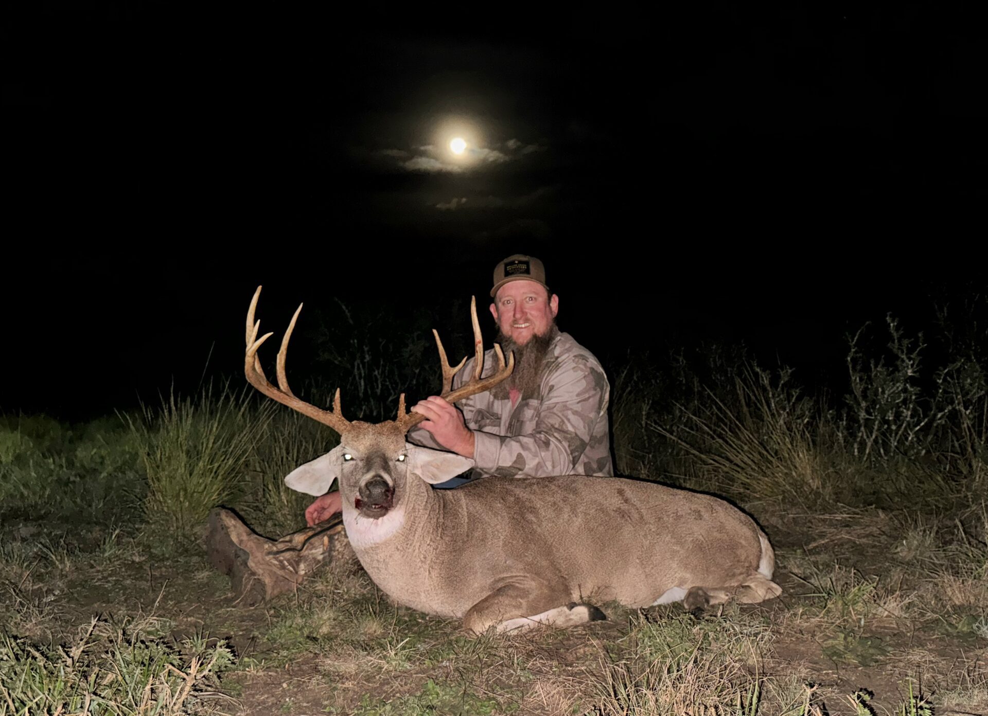 A man kneels beside a deer in a grassy field, showcasing a moment of connection with nature.